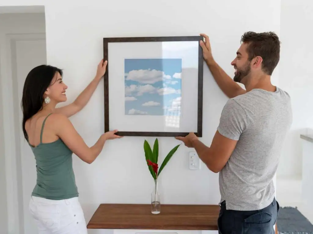 couple accrochant un tableau en verre au mur
